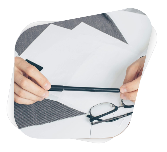 Close-up of hands holding a pen with papers and eyeglasses on a white table.